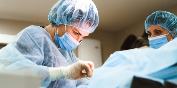 Team of medical professionals performing surgery while wearing protective equipment in a hospital setting.